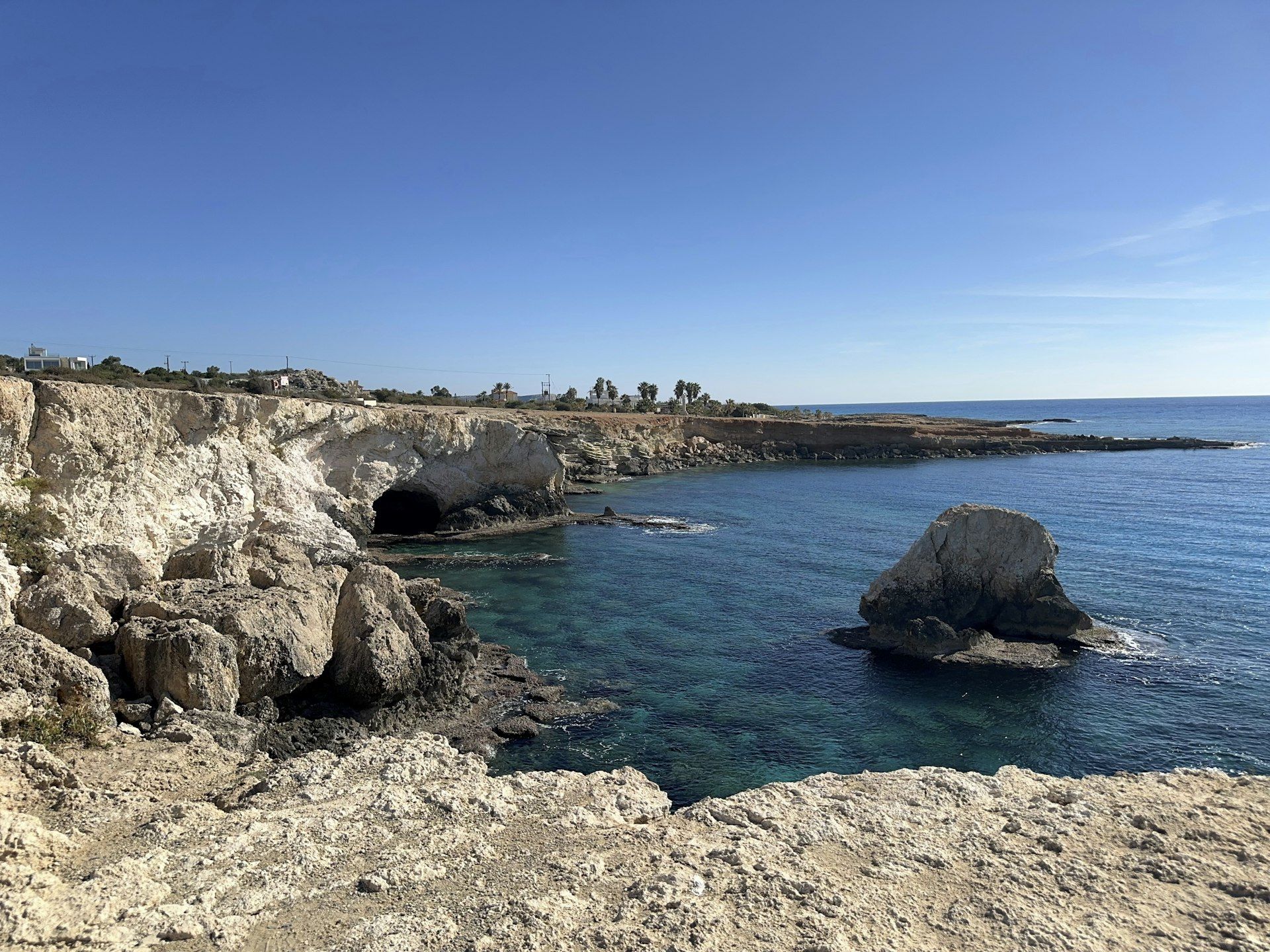 Coastal rocks and clear blue ocean under a blue sky.