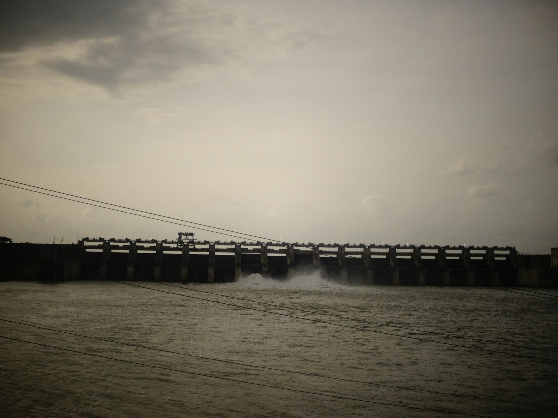 Water flows through a concrete dam under a cloudy sky.